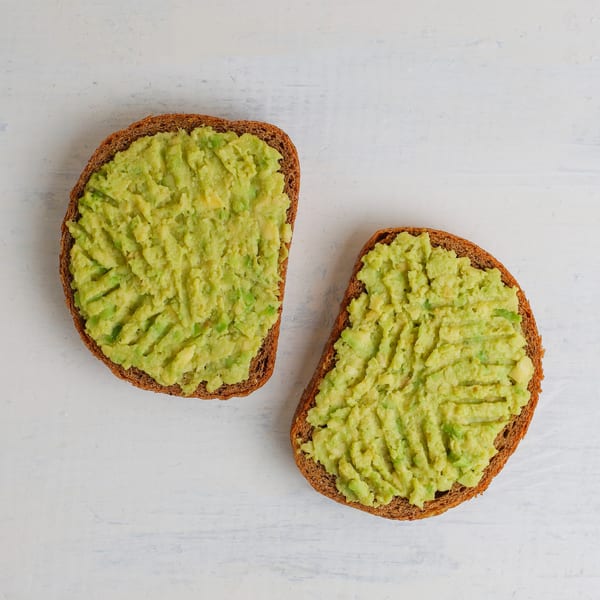 Two slices of dark bread topped with mashed avocado on a white wooden surface.