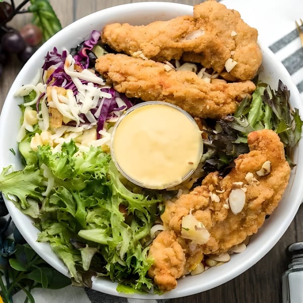 A Tastee Grill chicken tender salad with mixed greens, red cabbage, cheese, and dressing.